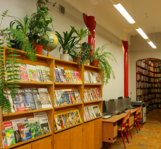 Po lewej stronie regały z czasopismami, na regałach rośliny doniczkowe i globus. Dalej wzdłuż ściany stanowiska komputerowe dla czytelników. W głębi widoczne przejście do kolejnego pomieszczenia.