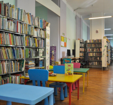 Po lewej stronie regały z literaturą dziecięcą, małe stoły i krzesełka dla dzieci, po prawej stronie lada biblioteczna. W głębi stanowisko komputerowe dla czytelników, regały z książkami dla dorosłych.